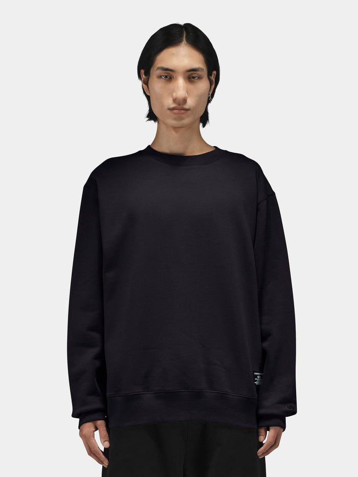 Alpha Industries Patched Crewneck in dark color with patch details, paired with black pants.