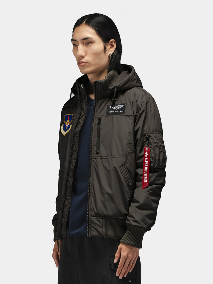 Alpha Industries Patched Hooded Rib Flight Jacket with military-inspired patches and red Remove Before Flight tag on pocket.