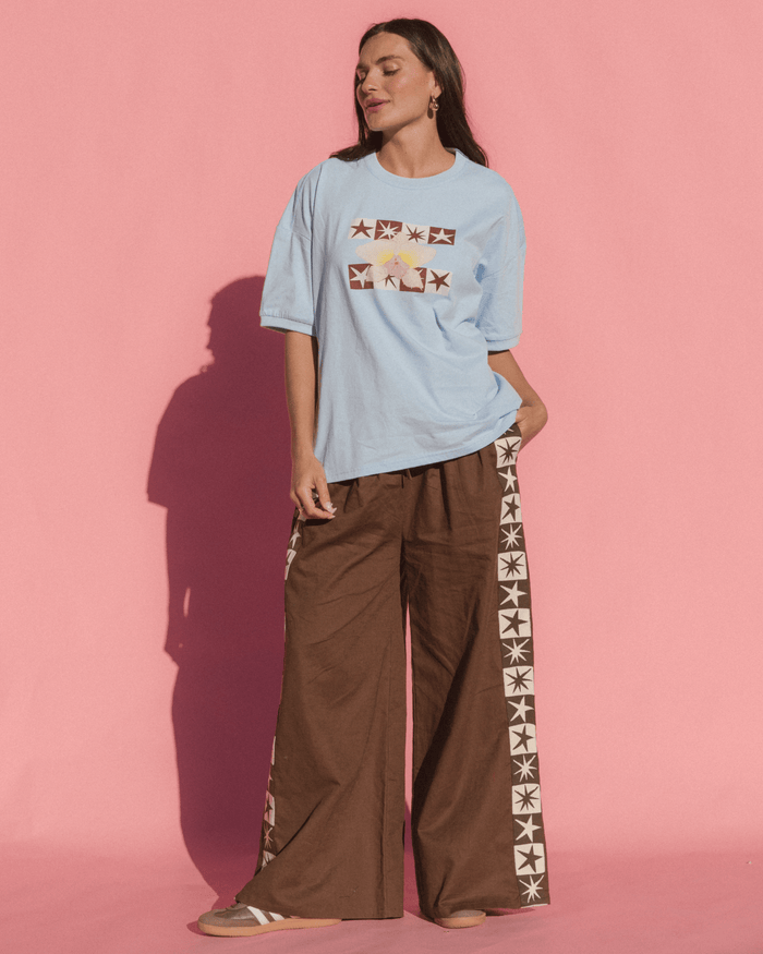 Woman wearing a light blue t-shirt and brown pants with star patterns against a pink background