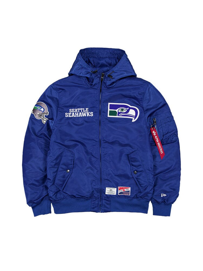 The Seattle Seahawks x Alpha Industries x New Era L-2B Bomber Jacket by Alpha Industries, in Pacific Blue, showcases team logos on the front, sleeve, and shoulder. This ripstop jacket includes pockets, a hood, and features a distinctive red zipper pull tag.
