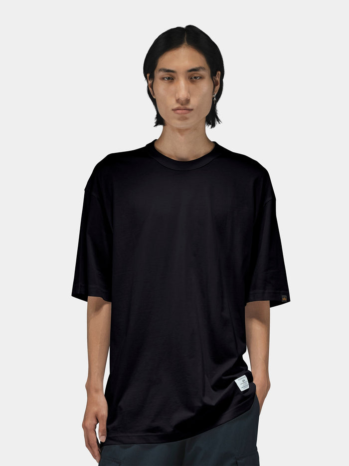 Alpha Industries Short Sleeve Relaxed Tee in black, features a crew neck and relaxed fit. Dark pants.