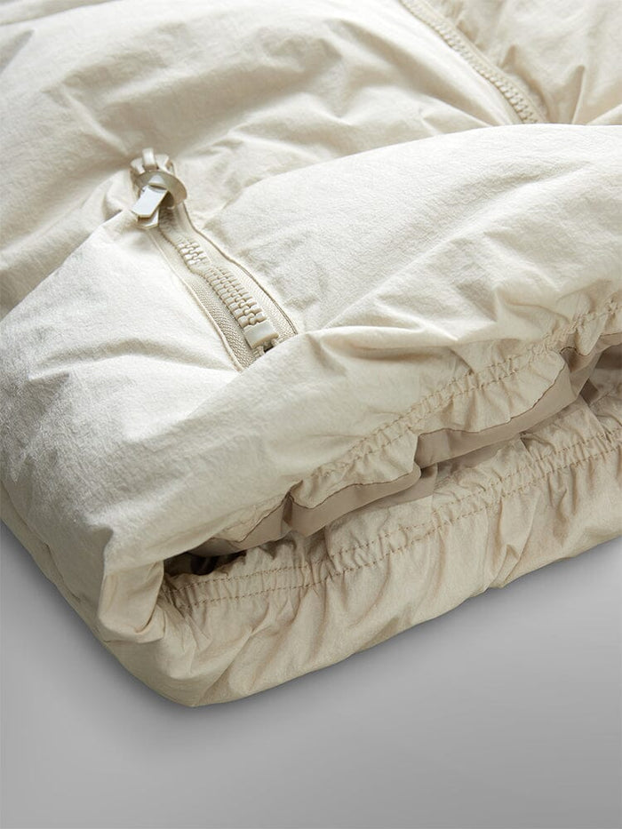 Sierra Short Puffer W by Alpha Industries, a beige puffer jacket with down fill and zipper, featuring an elastic hem, folded neatly.