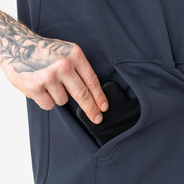 Front of hand pocket with man putting phone in tech pocket of the BRUNT sleeveless water resistant workwear hoodie in navy blue
