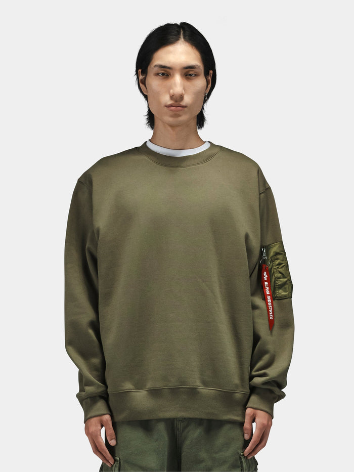 Alpha Industries Utility Pocket Crewneck in olive green with MA-1 zippered pocket, worn with cargo pants.