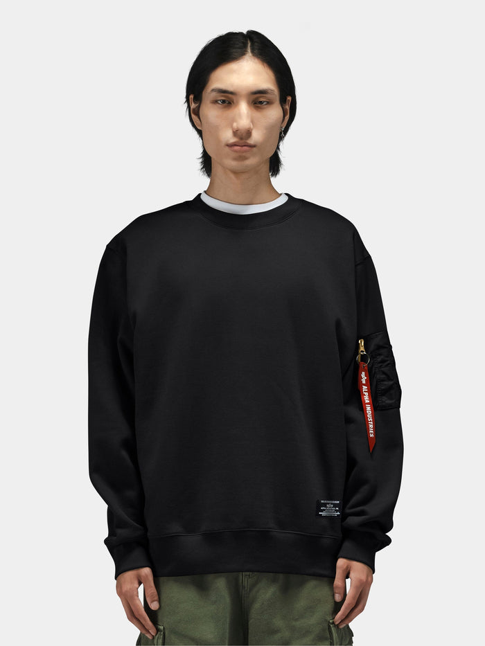 Alpha Industries Utility Pocket Crewneck with MA-1 utility pocket, logo embroidery on sleeve, and olive green pants.