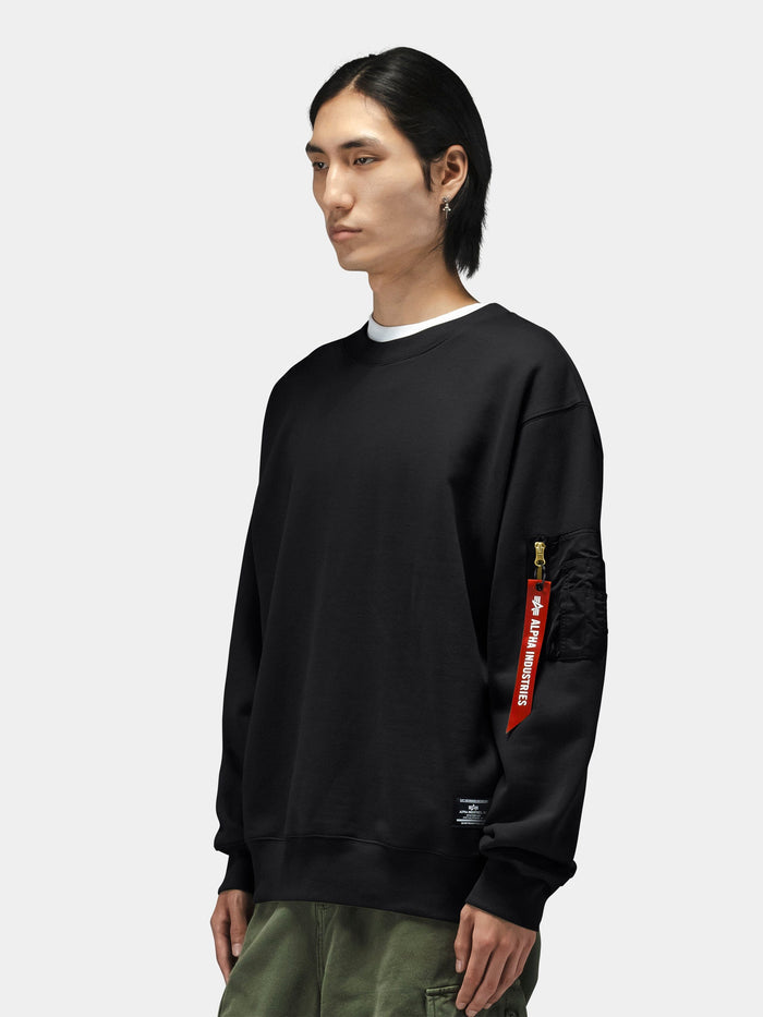 Alpha Industries Utility Pocket Crewneck with black MA-1 utility pocket and red tag, paired with olive green pants.