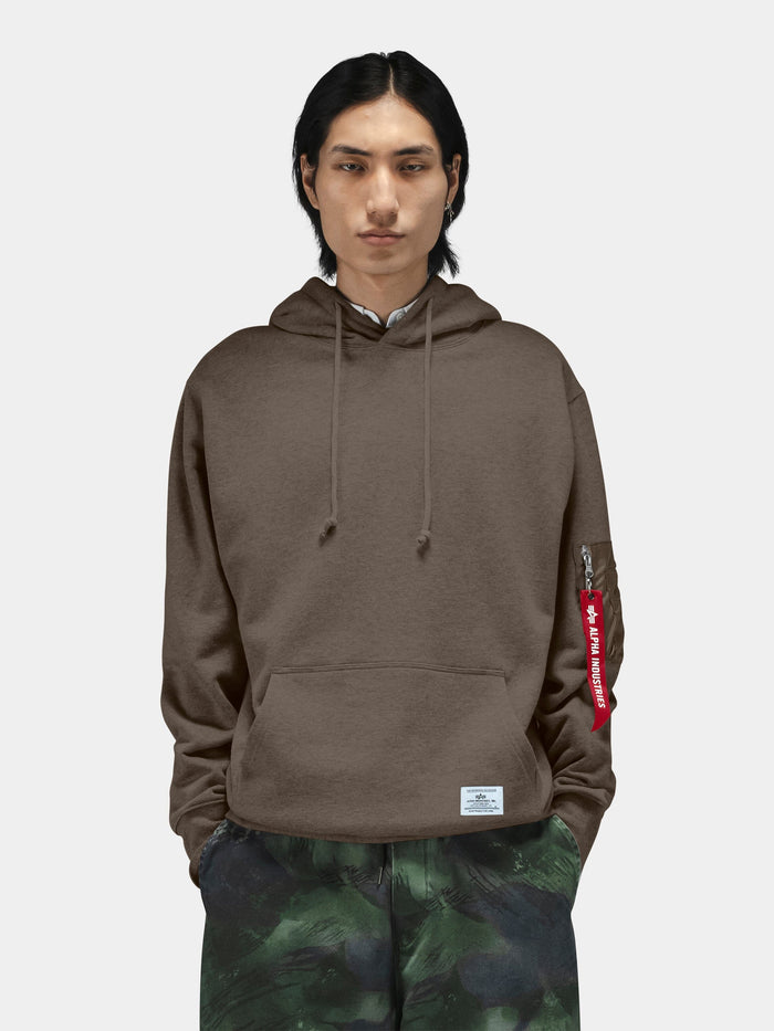 Alpha Industries Utility Pocket Hoodie in brown with utility sleeve pocket and red tag; green patterned pants.