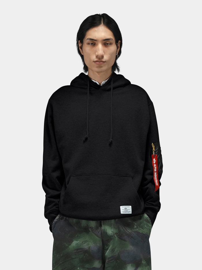 Alpha Industries Utility Pocket Hoodie with MA-1 sleeve pocket, paired with green camouflage pants.