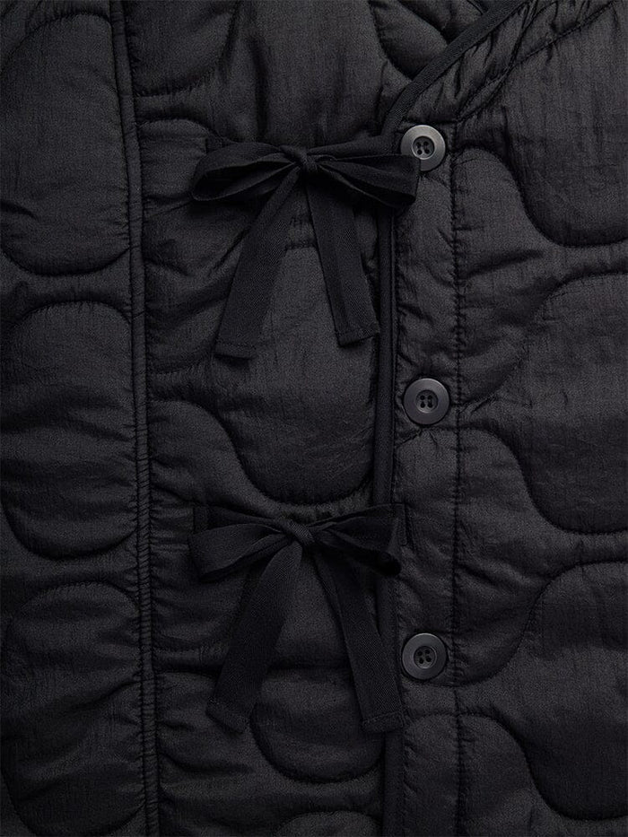 Close-up of the Women's Mixed Media Quilted Long Liner by Alpha Industries, showcasing its black quilted fabric adorned with two black bow ties and three vertically stitched black buttons in an onion quilting pattern.