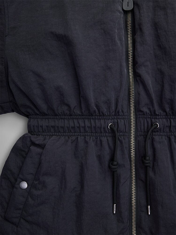 Close-up of the Alpha Industries Women's Short Cinched Waist Jacket in black nylon, showcasing a zipper, adjustable drawcord waist, and welt pockets. The design is enhanced with buttoned details and a cozy quilted lining.