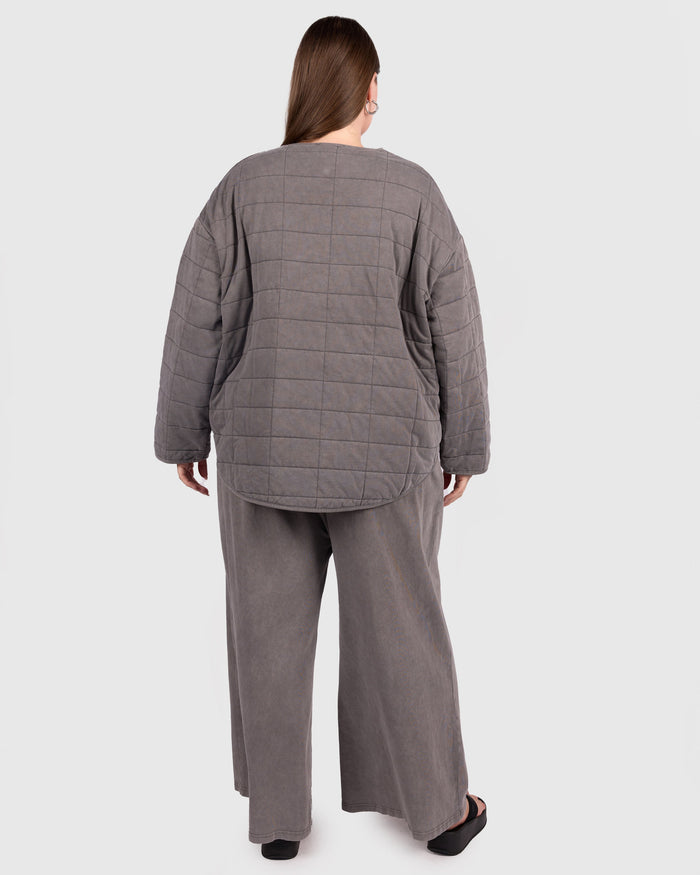 Person wearing a gray quilted jacket and pants on a white background